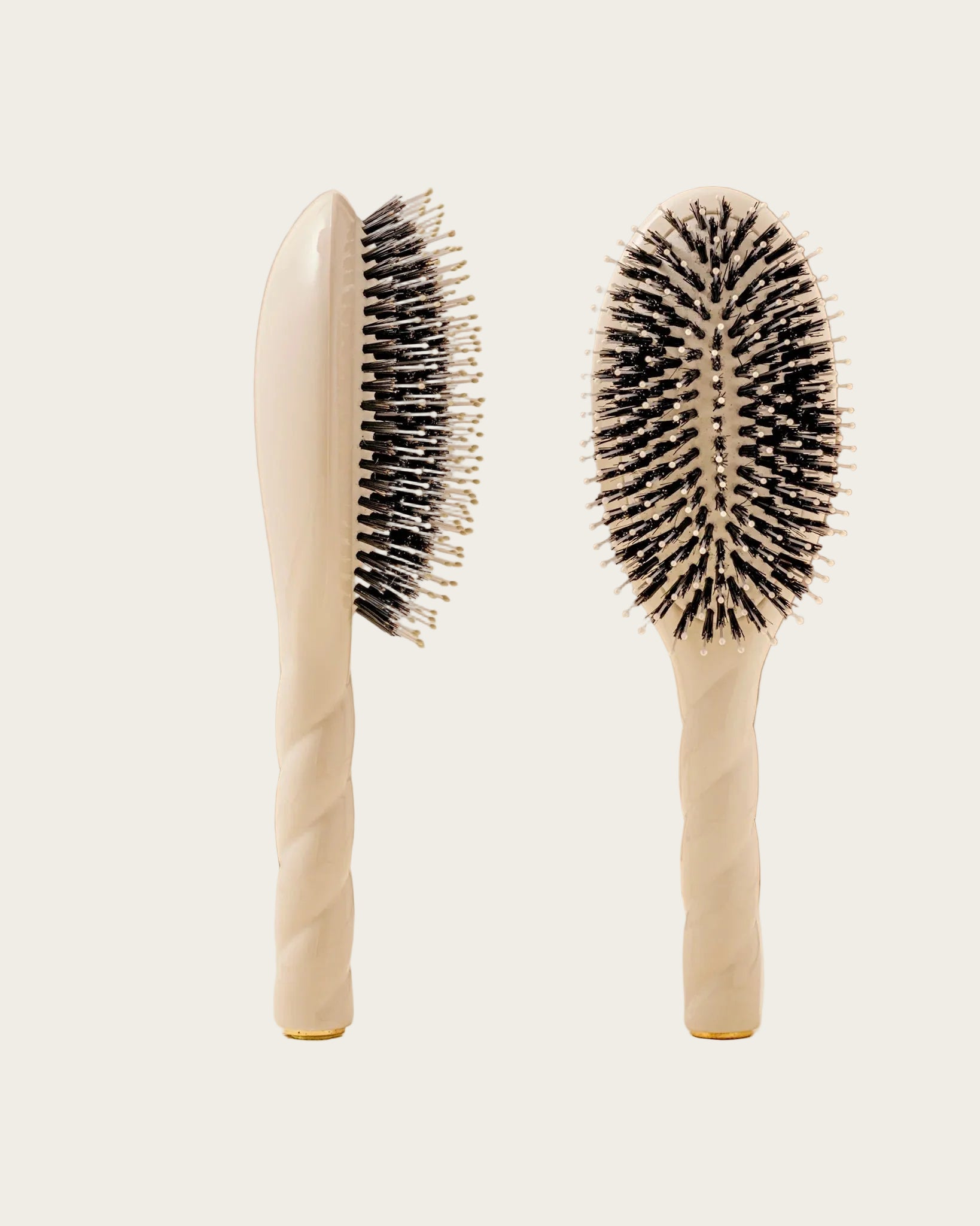 Two hairbrushes with black bristles on beige handles against a beige background