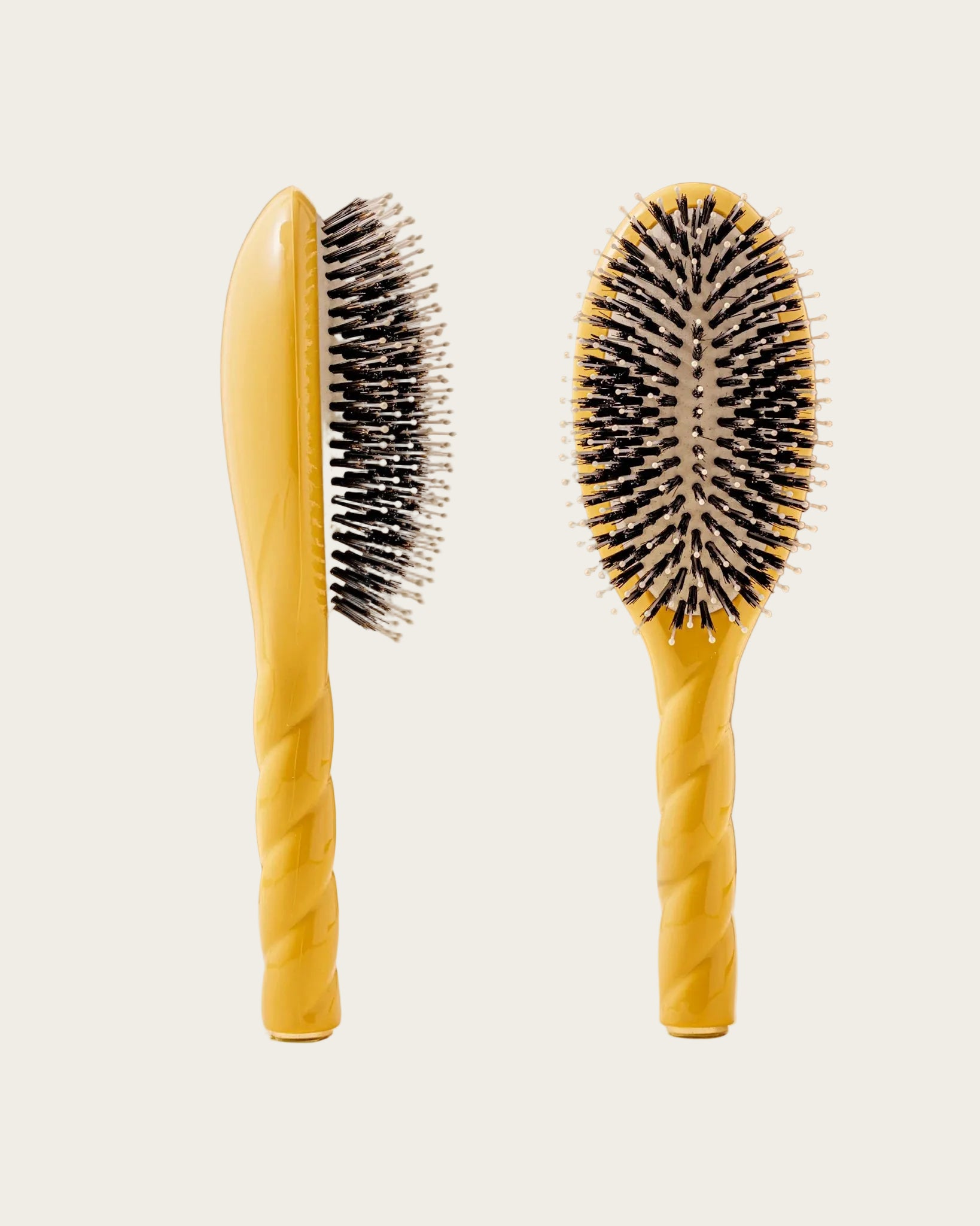 Two yellow hairbrushes with black bristles on a beige background