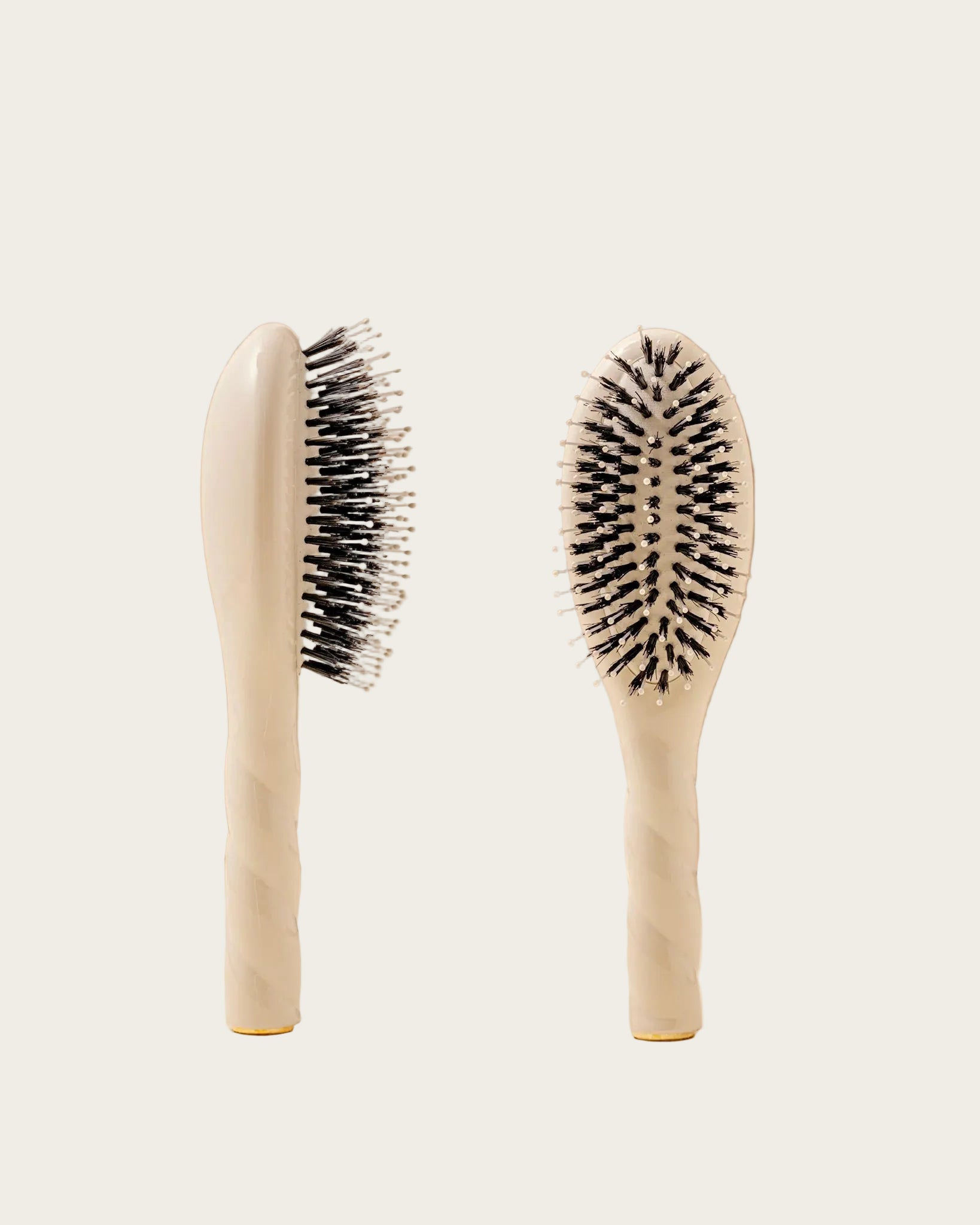 Two beige hairbrushes with black bristles on a beige background