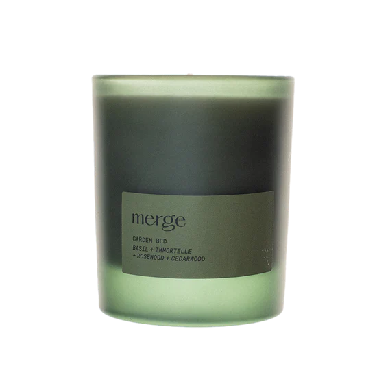 A green glass jar candle with a matching green label that reads 'merge' and 'Garden Rose + Ambrette + Rosemary + Cedarwood' on a white background.