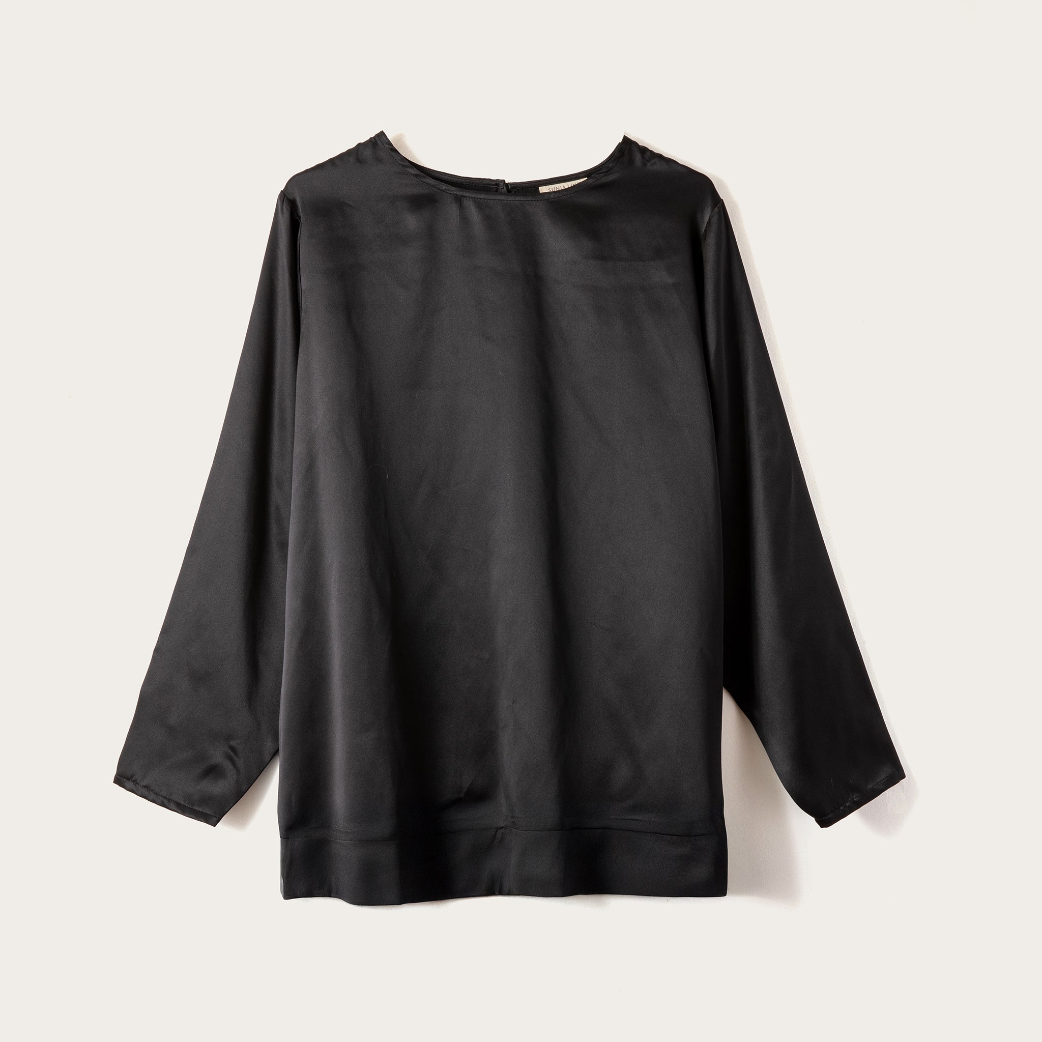 A black long-sleeve top with a crew neck, laid flat against a light beige background.