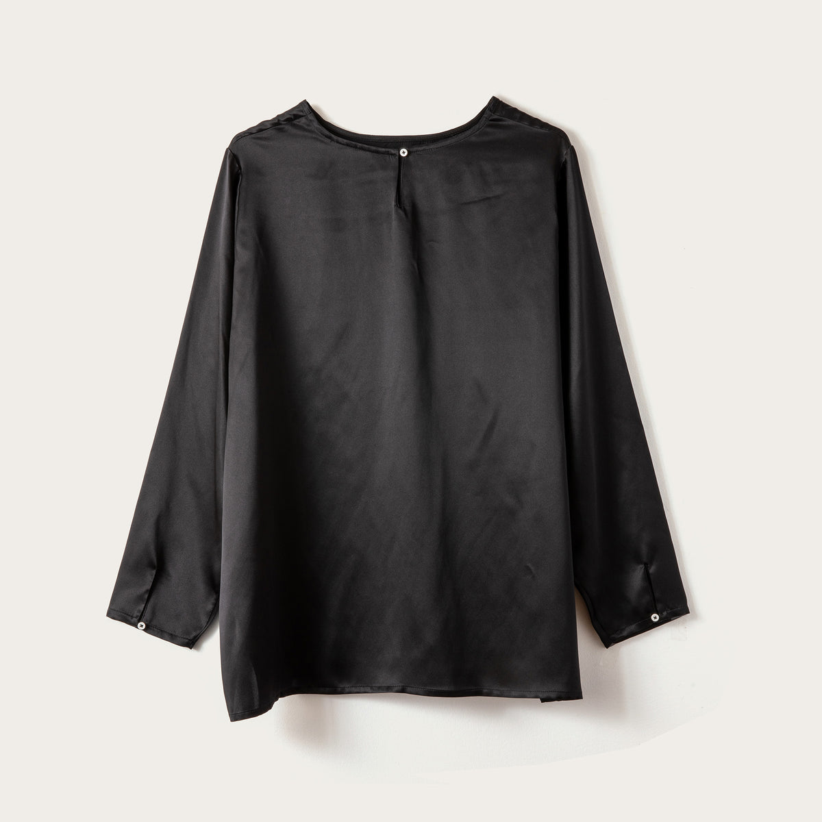 A black long-sleeve blouse with a crew neck and button details on the cuffs, displayed flat against a light beige background.