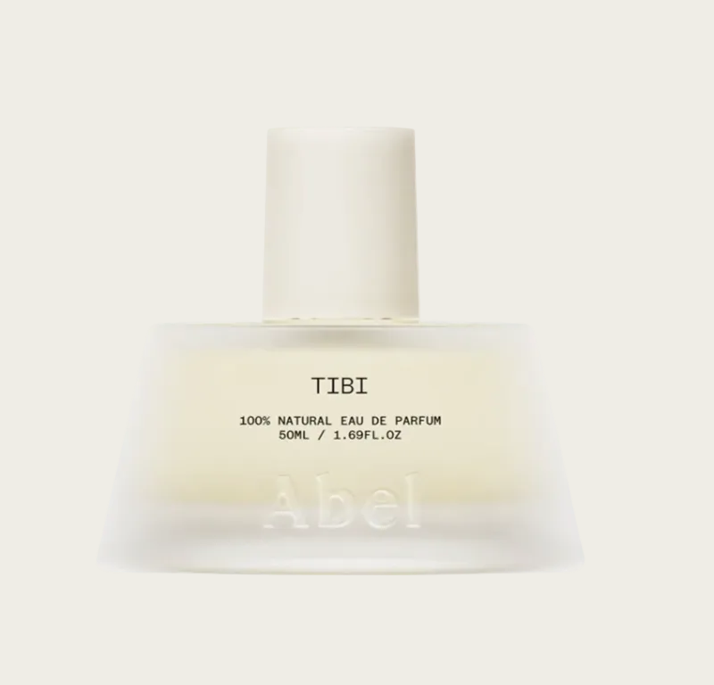 A frosted glass perfume bottle with a matte off-white cap, labeled 'TIBI 100% NATURAL EAU DE PARFUM 50ML' by the brand Abel, on a solid off-white background.