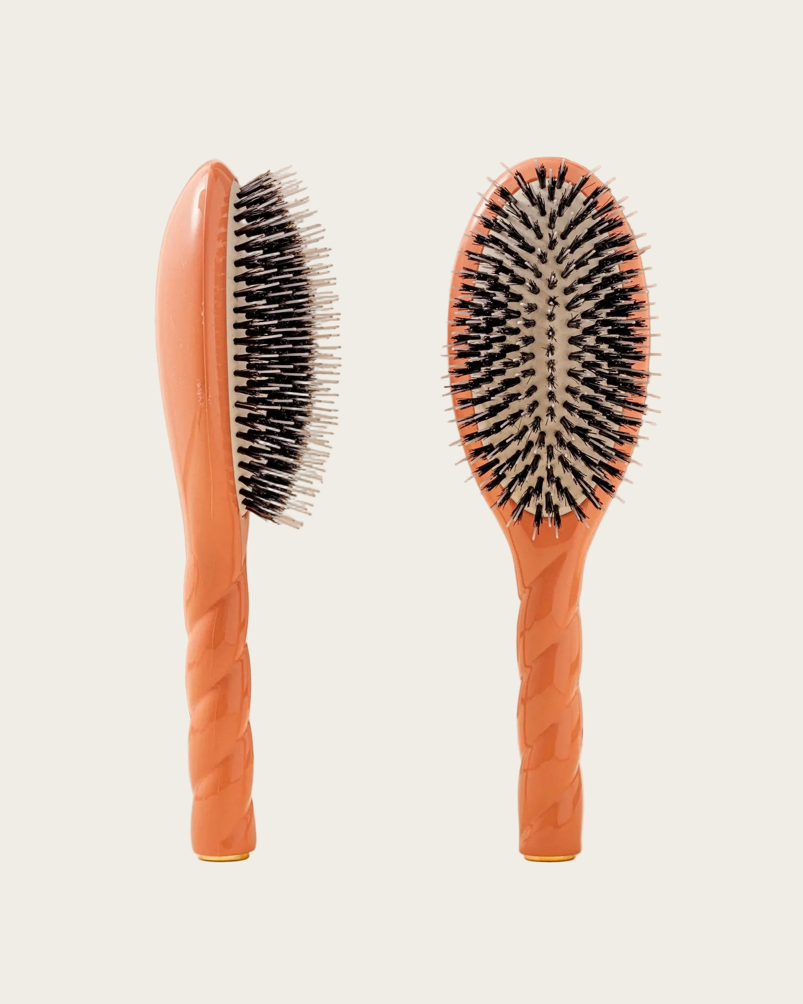 Two orange hairbrushes with black bristles on a beige background