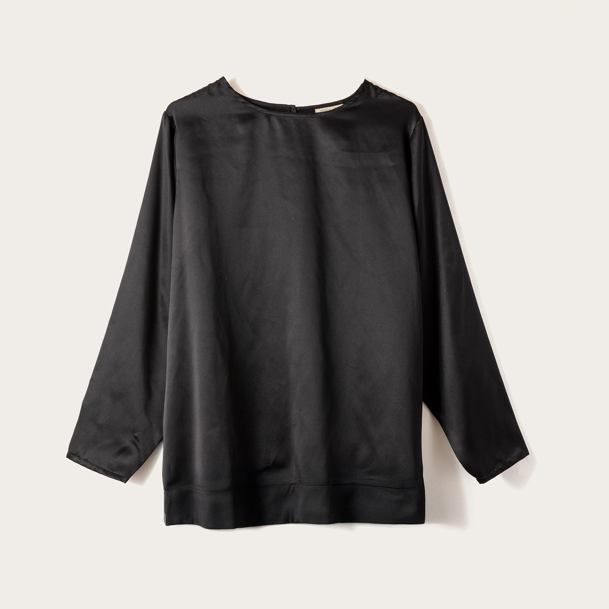 A black long-sleeve top with a crew neck, laid flat against a light beige background.