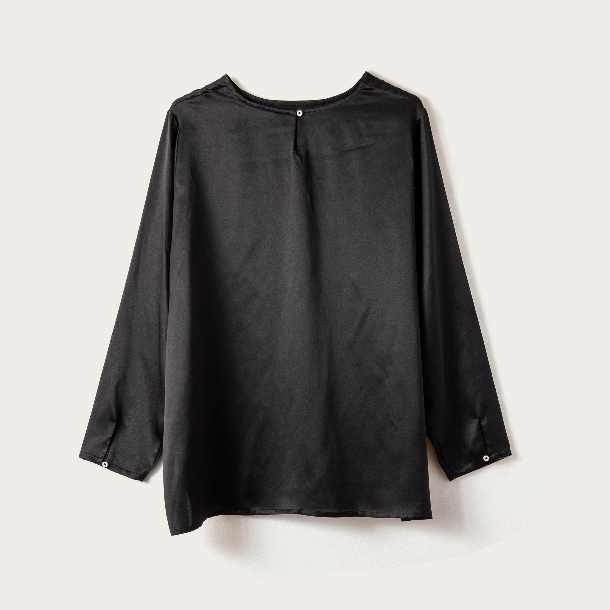 A black long-sleeve blouse with a crew neck and button details on the cuffs, displayed flat against a light beige background.