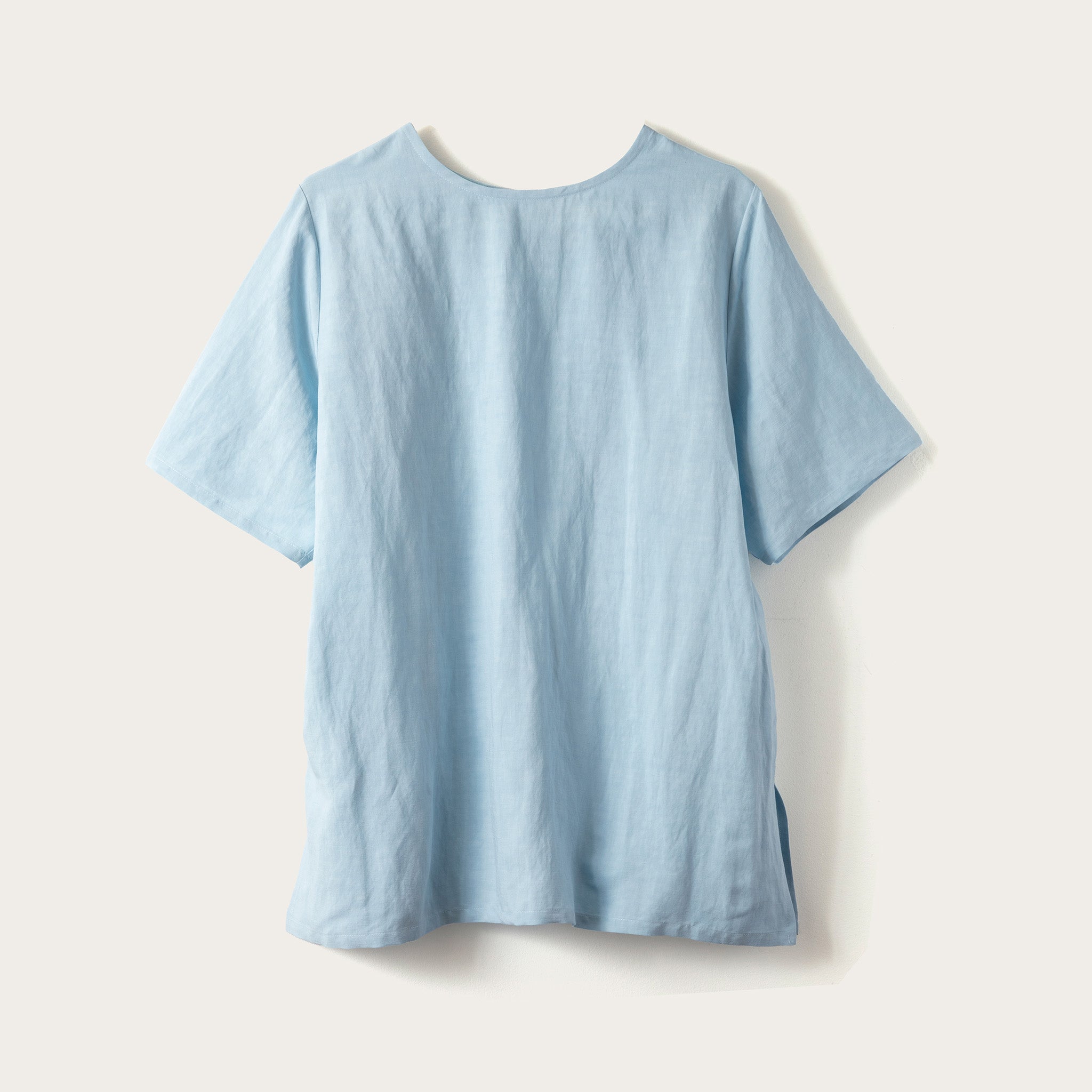 A light blue short-sleeve linen-blend t-shirt shown from the back, laid flat against a warm off-white background.
