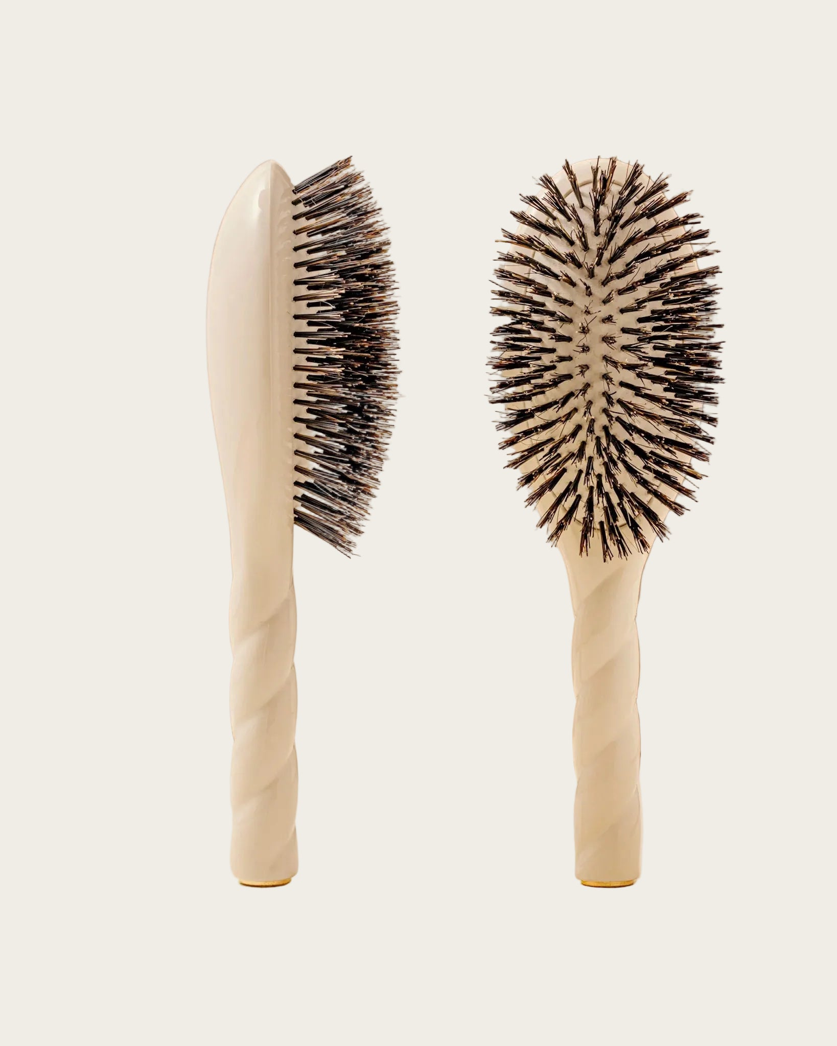 Two beige hairbrushes with black bristles on a beige background
